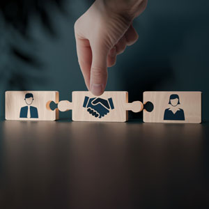Hand placing handshake puzzle piece between two figures, symbolizing mediation in Tennessee co-parenting disputes.